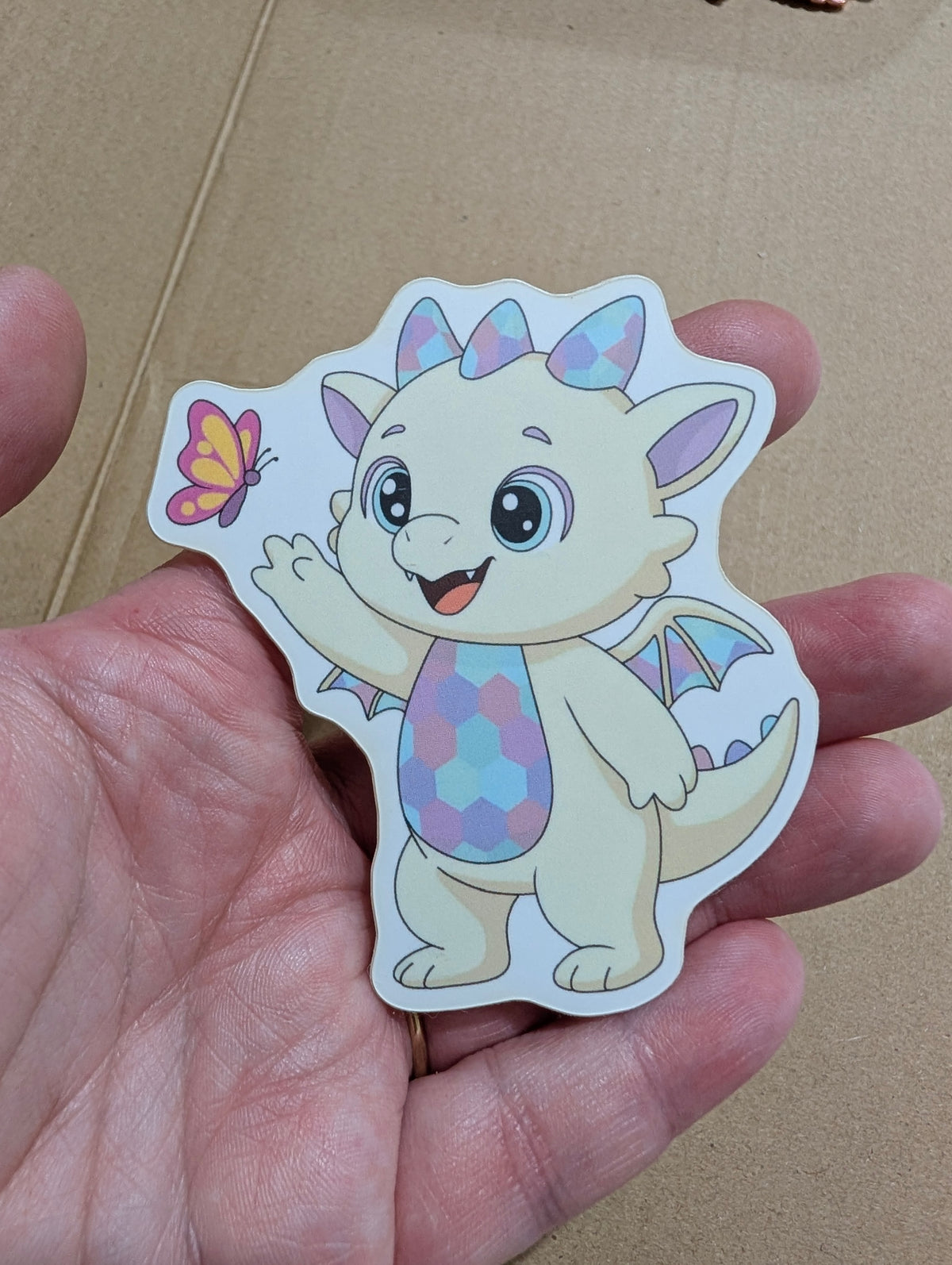 Opaliath die-cut sticker: a pastel baby dragon waving at a butterfly
