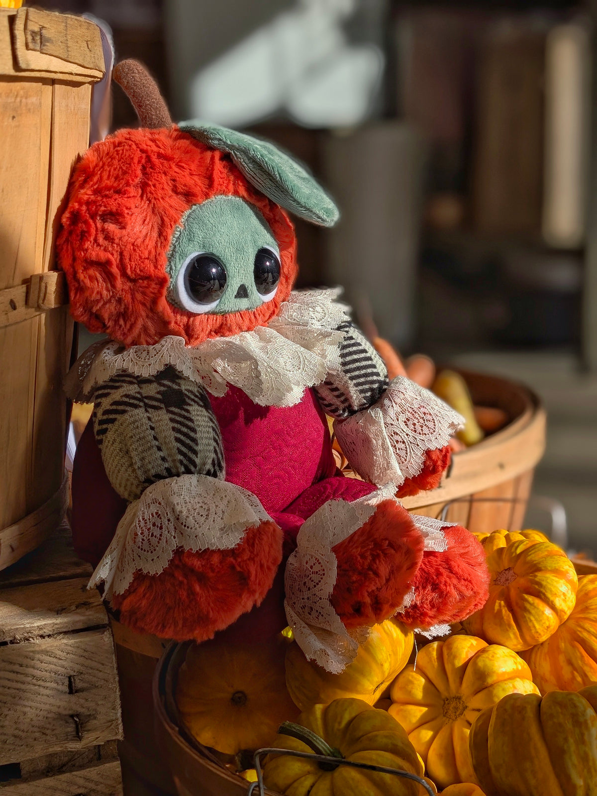 Ichabod, a one-of-a-kind pumpkin art doll with a vintage lace collar, sitting in warm sunlight at a farm stand