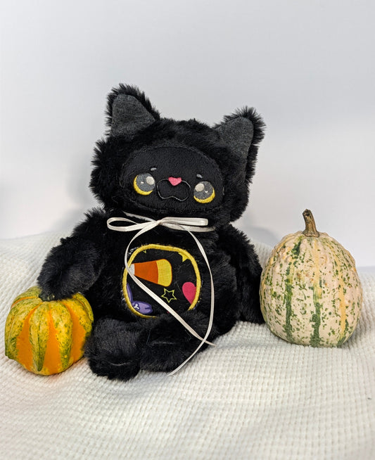 Licorice, a black kitty plushie with a white ribbon and candy corn belly
