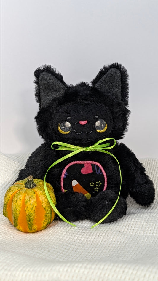 Tootsie, a black kitty plushie with a green ribbon and candy corn belly