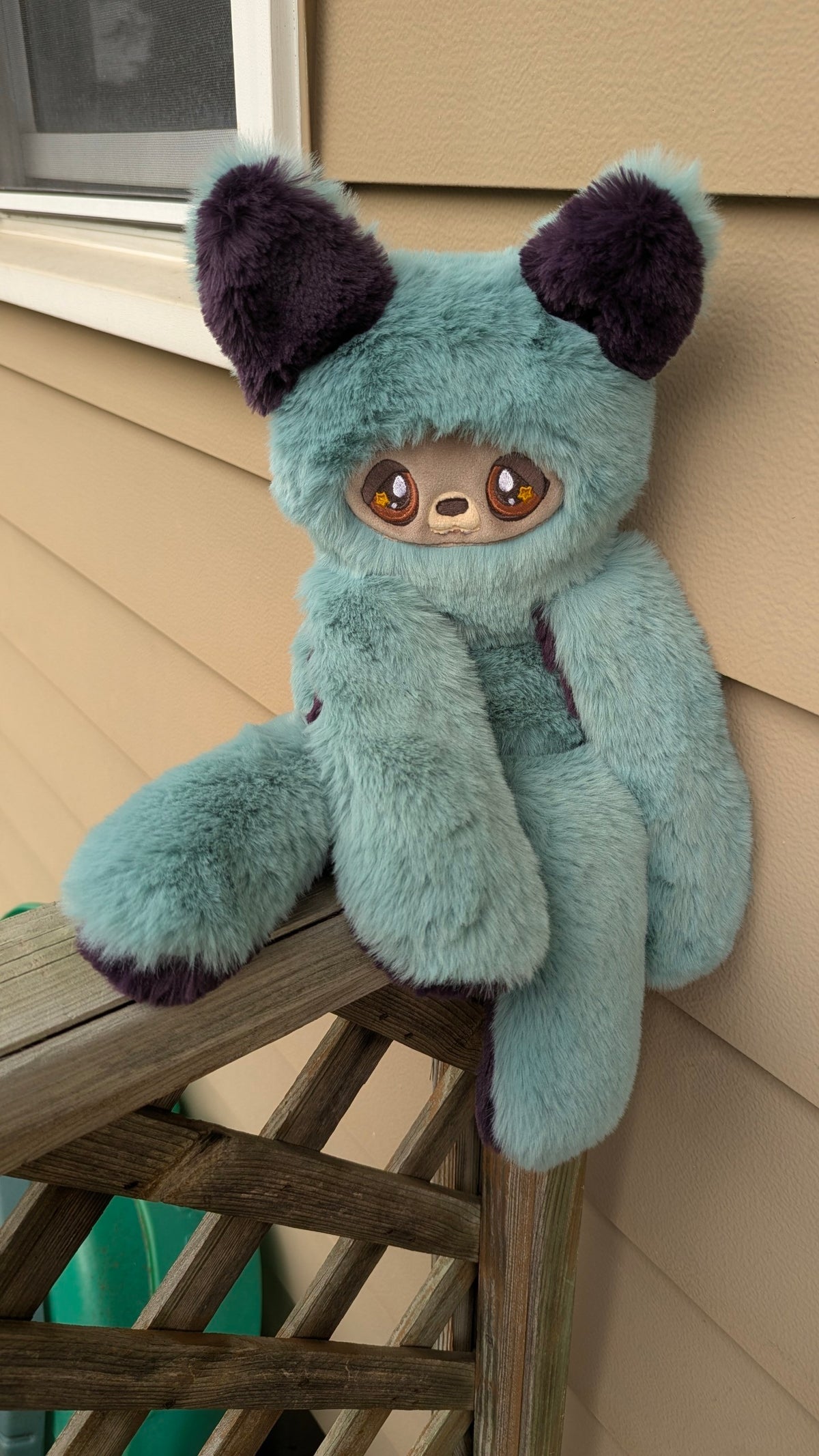 Evvies Lovies Jasper teal and plum plush wolf pup with amber star eyes and soft faux fur, sitting on a wooden railing.