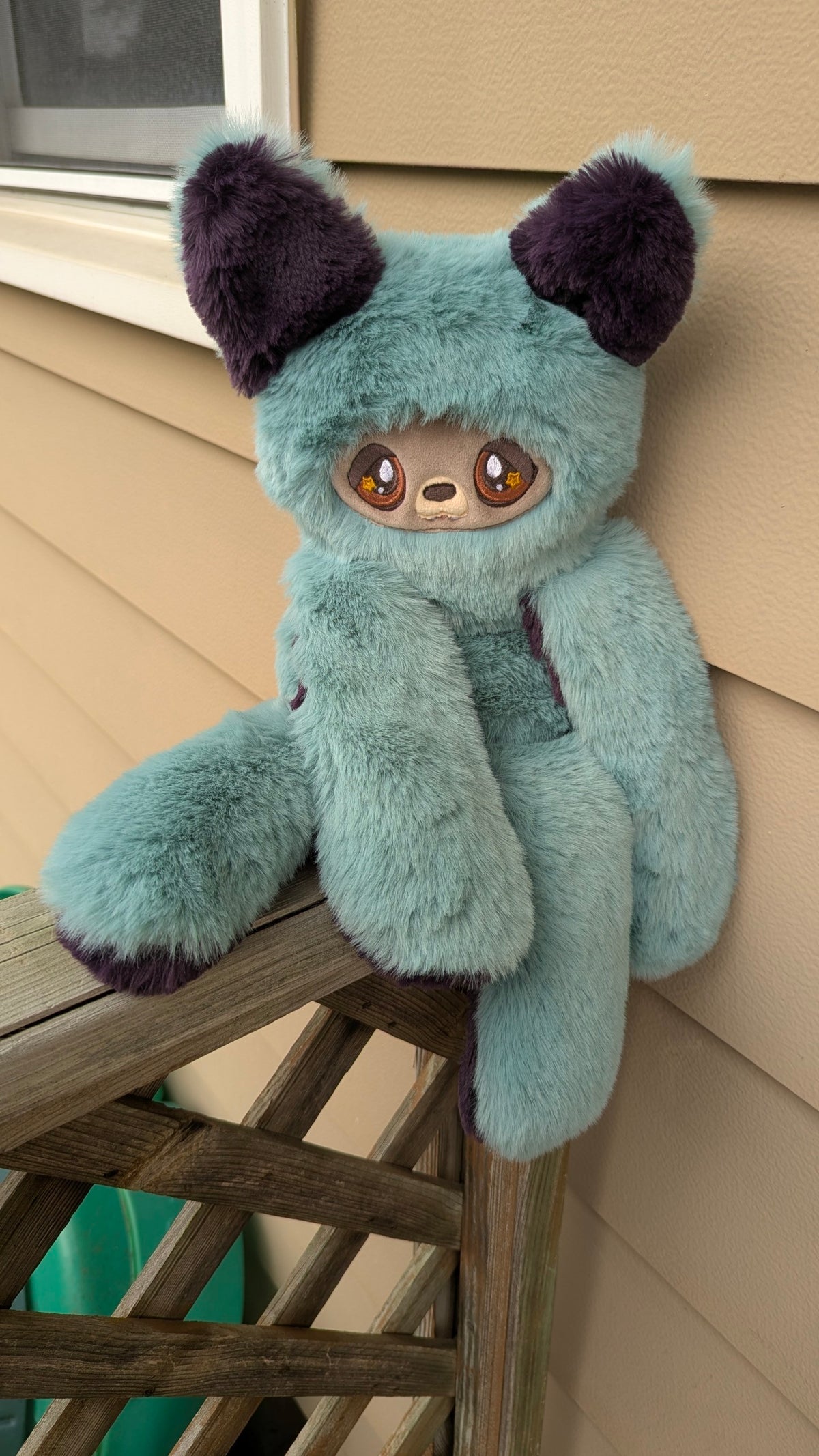 Evvies Lovies Jasper teal and plum plush wolf pup with amber star eyes and soft faux fur sitting on a wooden railing