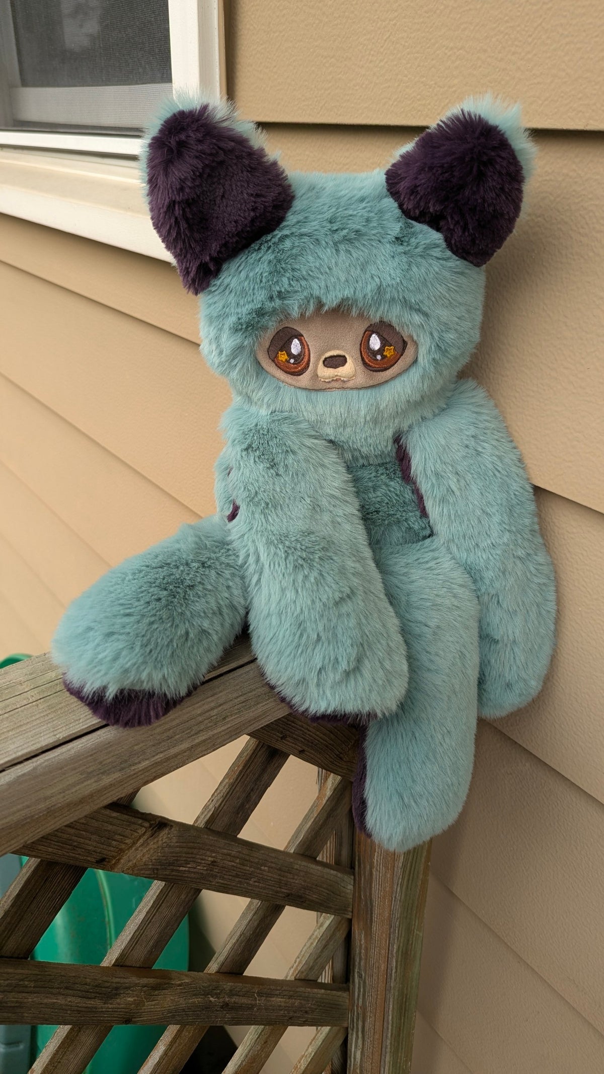 Evvies Lovies Jasper plush wolf pup with teal and plum faux fur, amber star eyes, and weighted paws on a wooden deck.